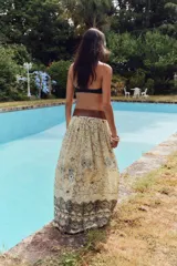 Falda larga color crema con estampado floral en tonos negro y dorado, cintura elástica con cordón ajustable y borlas decorativas.