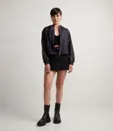 Campera cropped con capucha, de poliéster color negro con estampado de cuadros y salpicaduras de colores. Tiene cordón de ajuste en la capucha, elástico en puños y ruedo, bolsillos con cremallera y cierre frontal con cremallera.