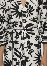 Blusa blanca con estampado floral negro, de tejido fluido, cuello de tira y cierre de lazo.