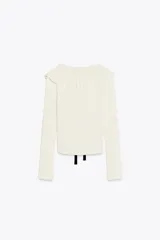Chaqueta blanca entallada de punto con cuello bobo de tricot y manga larga. Tiene una lazada negra en el cuello y cierre frontal con botones.