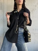 Camisa negra de corte oversize, con cuello clásico, manga larga y bolsillo en el pecho.
