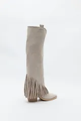 Bota texana de caña alta color beige confeccionada en gamuza, con punta fina, taco cuadrado de madera y detalle de flecos laterales. 