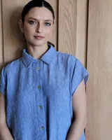 Túnica celeste de corte recto, con cuello camisero, mangas cortas, tajos laterales y cierre frontal con botones.