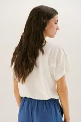 Blusa color crema con estampado de lunares negros, cuello redondo y mangas cortas.