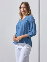 Blusa celeste de lyocell con cuello a la base y escote en V con apertura central y botones. Manga ¾ con puño y botón.