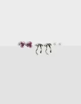 Set de tres pares de aros pasantes: un par de perlas, un par de flores color lila y un par de moños plateados.