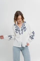 Camisa de manga larga en algodón liviano, color azul marino, con bordados florales en contraste en el frente y mangas. Cuello mao con terminación en ondas y puños fruncidos.
