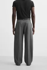 Pantalón gris de corte ancho con pliegues frontales y cinturón fino negro.