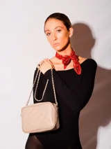 Bandolera clásica color beige, confeccionada en cuero natural, con diseño acolchado en forma de rombos. Posee correa de cadena entrelazada con cuero y cierre principal.