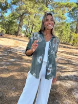 Camisa de algodón color verde militar con estampado floral en tonos claros. Presenta cuello camisero, botones frontales y mangas largas que se pueden remangar.