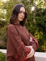 Buzo de algodón color blanco roto, de corte holgado, con puños y tajos laterales. Presenta un bordado artesanal en relieve de líneas orgánicas en color marrón caramelo sobre las mangas.