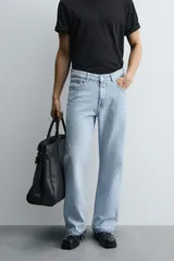 Pantalón de jean celeste de corte flare, con tiro medio, cinco bolsillos, cierre frontal con cremallera y botón, y bajo con acabado irregular.