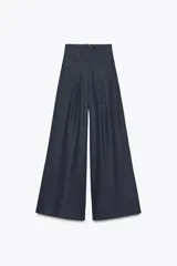 Pantalón de jean azul oscuro, de tiro muy alto y pierna ancha. Presenta pinzas en la parte delantera y cierre trasero con cremallera oculta.