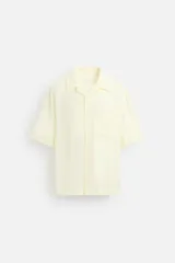 Camisa color amarillo claro, de corte relaxed fit, confeccionada en tejido fluido con mezcla de viscosa. Tiene cuello bowling, manga corta, bajo con aberturas laterales y cierre frontal de botonadura.