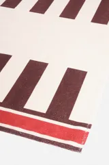 Toallón de playa blanco con rayas horizontales color bordó y logo "The Beach Club" estampado en rojo.