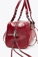 Bolso bowling color rojo con efecto craquelado. Tiene doble asa de hombro con detalles metálicos y asa bandolera extraíble. Incluye bolsillo interior con cremallera y cierre principal con cremallera.