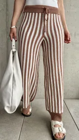 Pantalón tejido a rayas verticales color marrón y blanco, con cintura y tobillos acanalados con cordón ajustable.