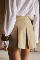 Falda pantalón color beige, de tiro alto, con bolsillos laterales tipo cargo, detalle de tablas y cierre lateral con cremallera oculta y trabilla con hebilla metálica.