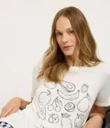 Conjunto de pijama de dos piezas compuesto por una remera de manga corta color blanco tiza con estampa de frutas en negro y un short estampado a cuadros en tonos azules y blancos.