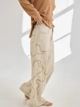 Pantalón de lino color beige con bordado artesanal de líneas onduladas en color marrón.