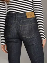 Pantalón de jean azul oscuro, de corte ajustado en la cadera y muslos, y acampanado a partir de la rodilla.