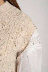 Chaleco de tejido de punto color beige melange con textura tweed y cuello redondo. Presenta un patrón de rombos calados y trenzas.