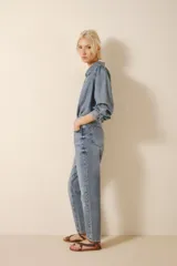 Jean de denim azul con lavado claro y efecto bigotes, tiro medio-alto y calce holgado con pierna recta que ajusta hacia el ruedo. Presenta bordado de alas en los bolsillos traseros.