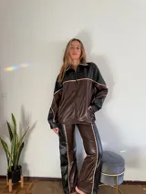 Conjunto deportivo de cuero sintético marrón y negro con detalles en rosa. Incluye campera oversize con cierre y pantalón acampanado.