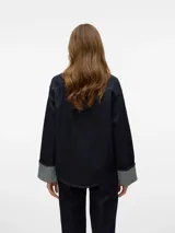 Camisa de jean azul oscuro con cuello clásico, cierre con botones plateados, mangas largas con puños con dobladillo y corte holgado.