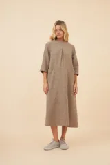 Vestido largo debajo de la rodilla, color marrón claro, con cuello bote, mangas 3/4 y bolsillos laterales. Prenda forrada con tajo en las mangas. Confeccionado en lana fina sin teñir, diseñado exclusivamente por Don Baez.