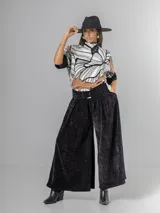 Pantalón ancho de corderoy negro con pliegues marcados en la parte delantera y cintura elástica. Incluye un cinturón negro con hebilla cuadrada.