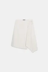 Minifalda pareo color blanco, de tiro medio y corte asimétrico. Se ajusta con lazos laterales.