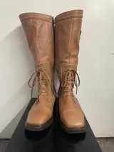 Botas de caña alta color marrón claro, hechas a mano en cuero, con cordones y cierre lateral.