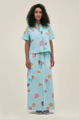 Falda larga de algodón color celeste con estampado de flores en tonos naranja, rosa y marrón. Es de corte recto, con tajo frontal, cintura ajustable con cordón y bolsillo lateral tipo cargo con solapa.