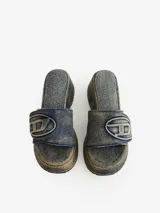 Sandalias de plataforma estilo mule, confeccionadas en denim de algodón lavado azul. Cuentan con una tira ancha ajustable con velcro que lleva el logotipo ovalado de Diesel en relieve. La suela es de plataforma gruesa con tacón curvo y banda de goma dentada.