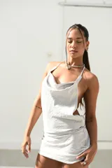 Vestido corto plateado con escote drapeado tipo cowl neck y tirantes finos. Presenta un corte ajustado y aberturas pronunciadas en los laterales.