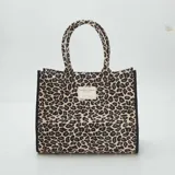 Bolso shopper con estampado de leopardo en tonos beige y negro, con asas cortas y etiqueta con texto en el frente.