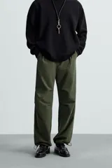 Pantalón verde militar de corte relaxed fit confeccionado en tejido técnico ligero. Cuenta con cintura elástica ajustable con cordón interior, bolsillos frontales y traseros con solapa, pliegues en las rodillas y bajo ajustable con elástico.