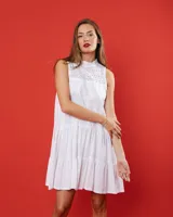 Vestido blanco de largo por arriba de la rodilla, con cuello alto y cierre invisible en la espalda, canesú de broderie y cuerpo de lino con volados.