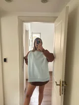 Buzo celeste con mangas marrones y bordado dorado en el frente.