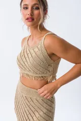 Musculosa tejida color dorado con diseño calado y flecos en el ruedo.