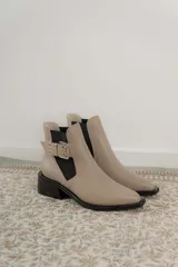 Botines Chelsea color beige con elásticos laterales negros, punta cuadrada, detalle de hebilla lateral y tacón bloque bajo.