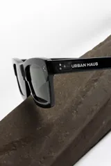 Lentes de sol negros con marco rectangular y lentes verdes.