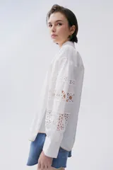 Camisa blanca de popelina con calce recto y levemente holgado. Mangas largas con galones florales y bordes festoneados en beige.