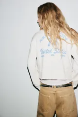 Sudadera corta color blanco hueso, de cuello redondo y manga larga. Tiene un estampado con la frase 'IN MY YEEHAW ERA' en color negro.