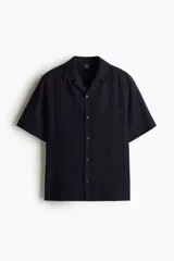 Camisa negra de manga corta con cuello resort, tapeta lisa, bolsillo superior y canesú en la espalda.