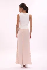 Pantalón de tela color rosa pálido, de corte palazzo y cintura alta con elástico. Presenta aberturas circulares verticales en los laterales.