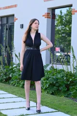 Vestido corto negro con escote en V, sin mangas, corte a la cintura con faja de lentejuelas y falda acampanada. 