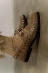 Mocasín de cuero color marrón con tachas metálicas plateadas en la puntera y laterales.