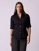 Camisa negra de algodón con cuello clásico, escote en V y mangas 3/4 con trabillas y lazos. Tiene dos bolsillos con solapa en el pecho y cierre frontal con botones.